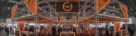 Large orange-lit truss exhibition structure with a busy show floor